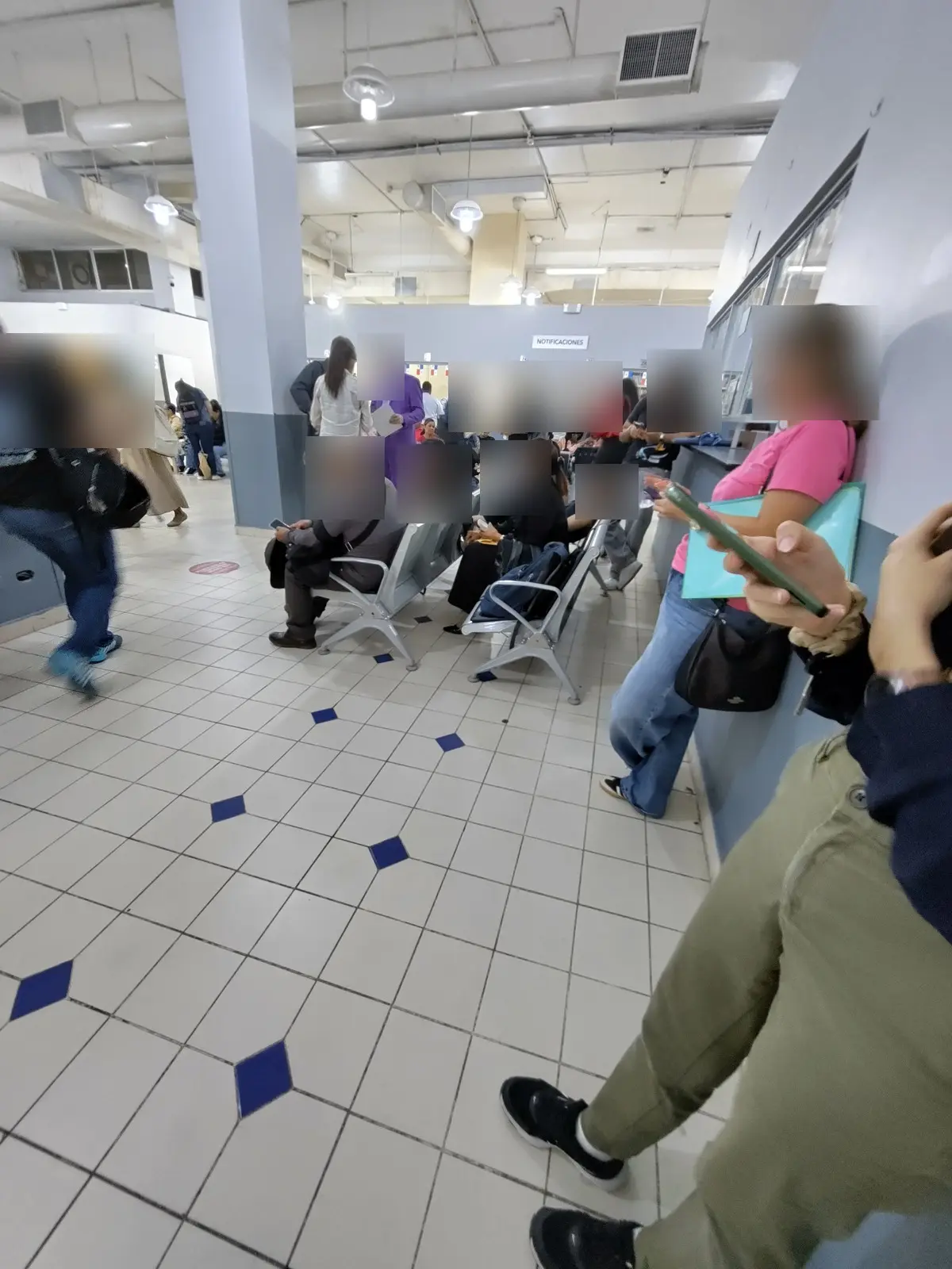 Waiting hall of the Servicio Nacional de Migración, Notificaciones sign in the back (faces blurred)